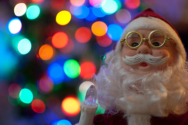 Santa with Christmas tree behind him shot with my 35mm f/1.8 at f/1.8. Note the smooth, even out-of-focus highlights, though they tend to get football-shaped near the corners of the image.