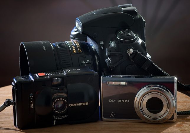 The Olympus XA is pictured with an Olympus FE-5020 and the full-size DSLR, the Nikon D700.