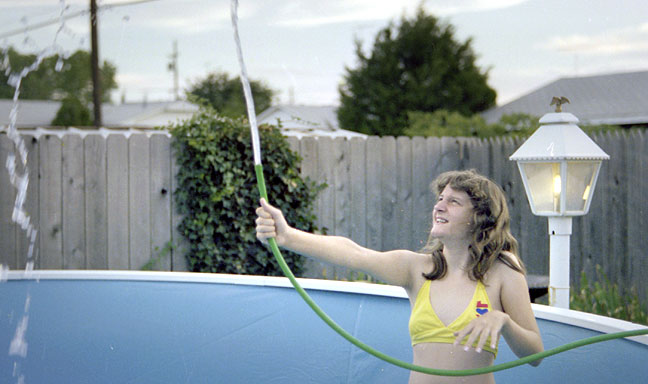 My sister Nicole plays with a garden hose as our new backyard pool begins to fill with water, July 1978.