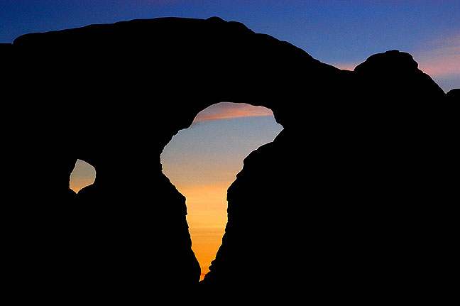 Turret Arch is silhouetted against the sky after sunset at Arches National Park.