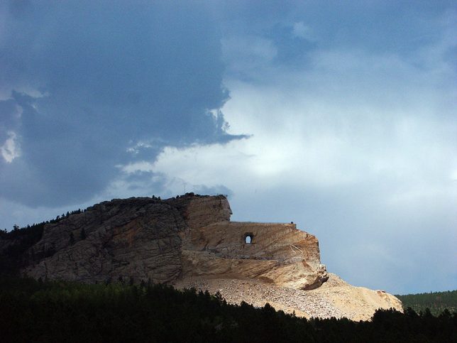 This broad view of the Crazy Horse Memorial shows its enormity beneath a thunderstorm.