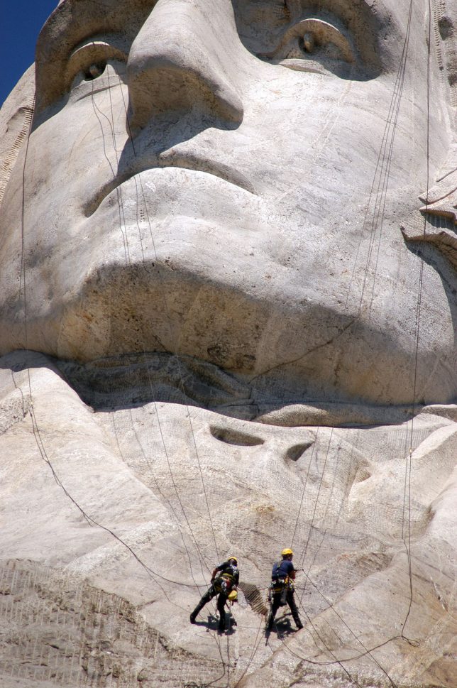 Workers dangle on the faces of Mount Rushmore as they power wash the attraction.