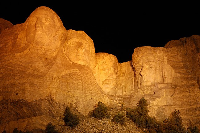 The faces on Mount Rushmore are illuminated by deep amber light during the nighttime ceremony at the Monument.