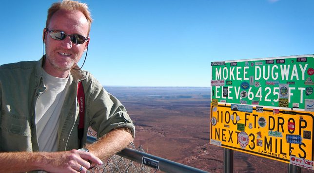 Your host poses at the sign at the top of the Mokee Dugway. Just three years earlier, this sign had no stickers on it.