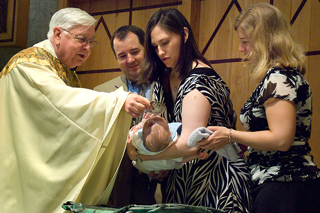 Tom and Chele hold their son Paul Thomas as a priest baptizes him during the Christening ceremony. Assisting is Tom's sister Rose.