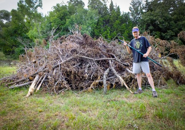 Your host poses with a rake by his giant brush pile of branches cut, sawed, and dragged over a three-week period. 