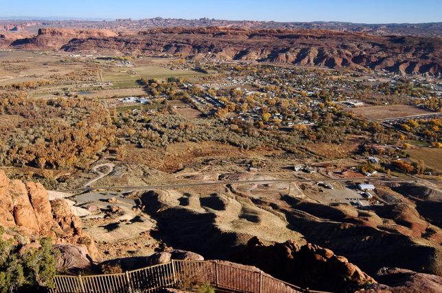 The City of Moab, Utah is laid out before visitors to the Moab Rim, with Arches National Park on the horizon.