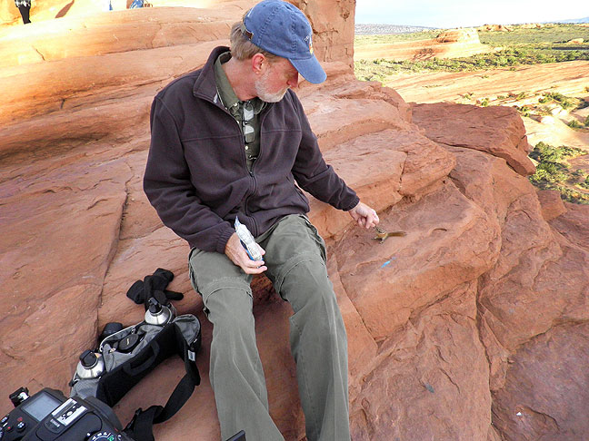 A fellow traveller used my camera to make this image of me greeting a chipmunk as the light matured after sunrise at Delicate Arch.