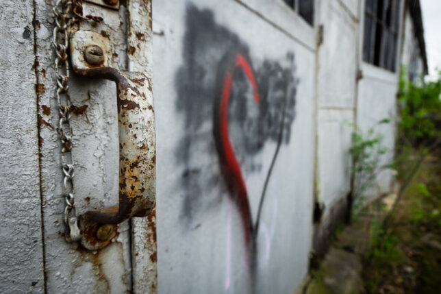 The nearly colorless rusted handle on a sliding door at a warehouse in Picher, Oklahoma is contrasted against a bright red heart graffito tag.
