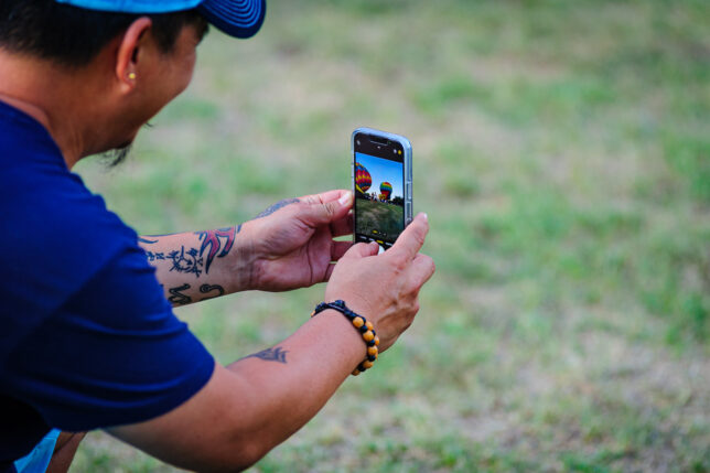 A man uses a smartphone to photograph friends and relatives in the balloon field as dusk approaches.