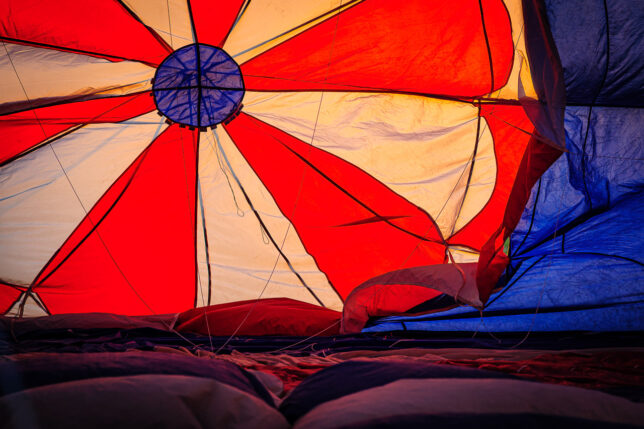 Sunset light shines through the top of a balloon as the crew inflates it. This part of the balloon is a large, round flap called a "parachute valve," and can be opened by a rope in the gondola to release hot air and allow the balloon to descend.